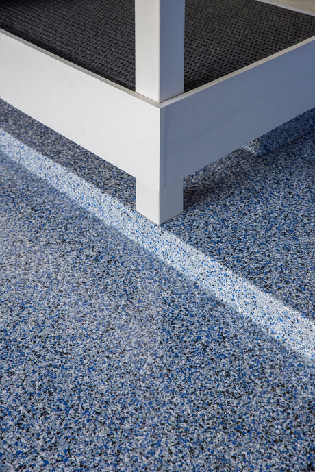 Blue and gray color flake broadcast on an epoxy floor beside a white wall.