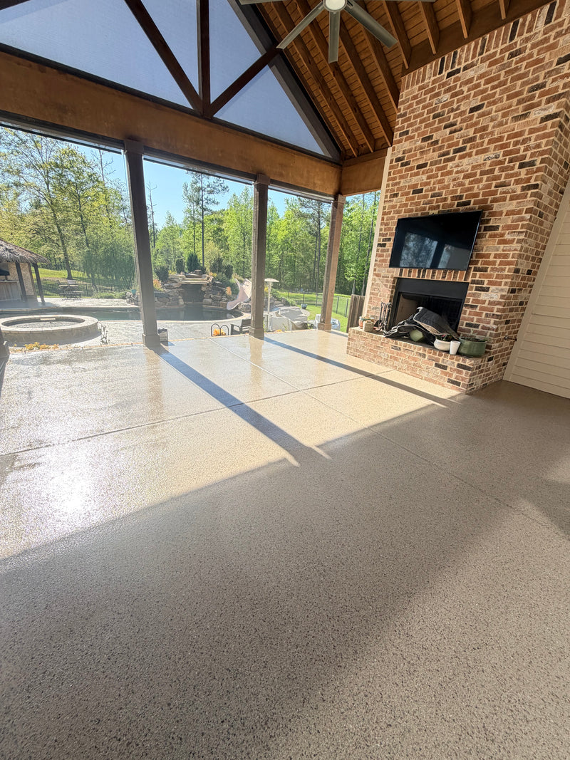 Tan flake epoxy floor on a covered patio with a brick fireplace and pool view